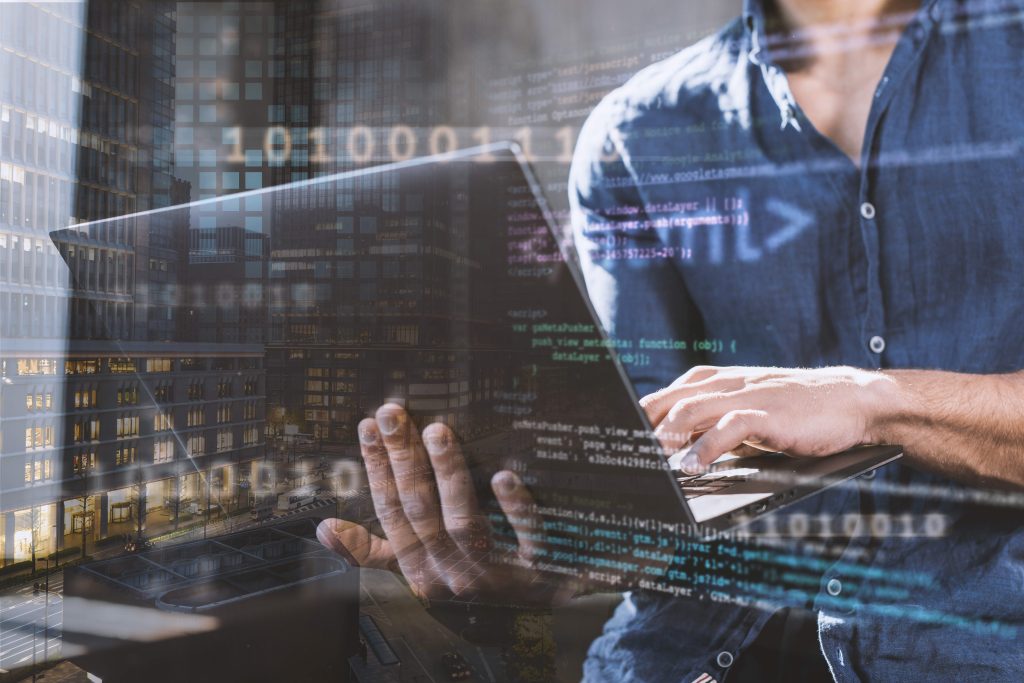 A person working on a laptop with code and city buildings in the background, symbolizing tech and innovation.