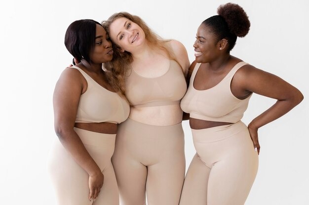 Three confident women smiling and posing in stylish body shaper outfits.