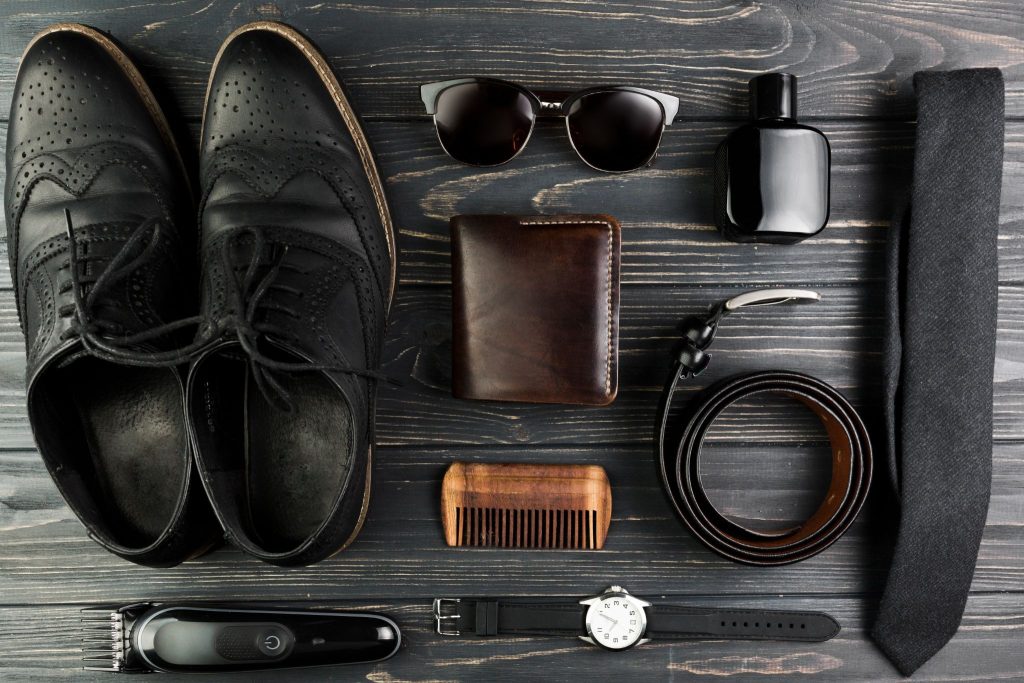 Men's accessories with shoes, tie, wallet, belt, watch, sunglasses and grooming items on dark wood background